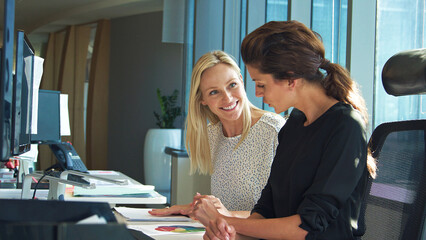 Two Female Business Colleagues Sitting At Desk In Office Discussing Documents