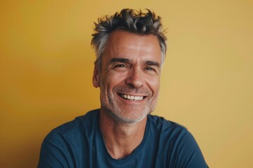 Obraz premium Portrait of a tender caucasian man in his 50s smiling at the camera in front of pastel yellow background