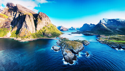 Obraz premium Coastal Paradise: A breathtaking panorama of a rugged coastline with majestic mountains, vibrant green vegetation, crystal clear blue water under a bright blue sky. 
