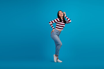 Young woman posing with happiness in a stylish striped shirt against a blue background, embracing...
