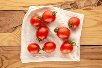 Juicy cocktail tomatoes with a white linen napkin, on a wooden table, close-up, top view.