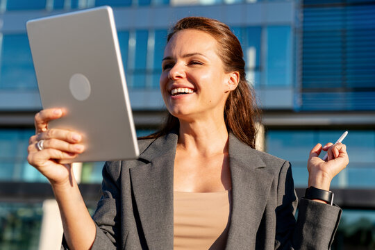 Joyful female business person using her digital tablet outside the office building and smiling.