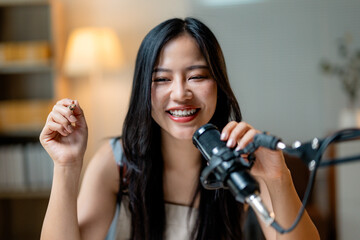 Young woman vlogger recording audio podcast, talking in microphone, gesturing and smiling