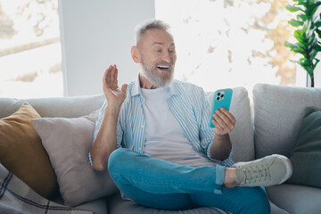 Elderly Man Enjoying a Video Call on Smartphone While Relaxing on a Sofa in a Bright Contemporary Living Room
