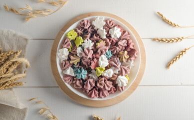 Multi-colored mini meringues on a plate on a white wooden background, flat lay