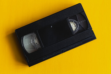 Obraz premium A single video cassette on a bright yellow background — a minimalist yet expressive symbol of the bygone VHS era. This image can be associated with retro style, vintage culture, and nostalgia.