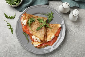 Delicious crepes with salmon, cream cheese and arugula on grey table, flat lay