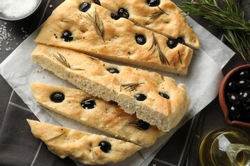Slices of delicious focaccia bread with olives, rosemary, oil and salt on grey table, flat lay