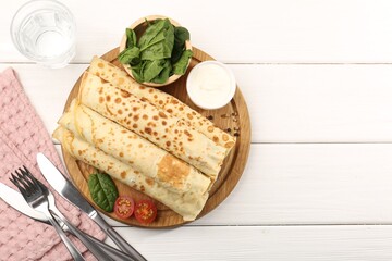 Tasty rolled crepes with cottage cheese and spinach served on white wooden table, flat lay. Space for text