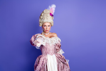 Young woman dressed in ornate royal costume pointing forward on purple background