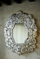 Interior decorative detail of a mansion, mirror with a large silver baroque style frame on warm gray wall background