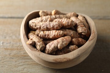 Raw turmeric roots in bowl on wooden table, closeup