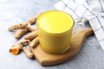Tasty turmeric latte in cup and roots on grey table, closeup