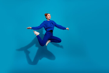 Energetic young woman in vibrant blue outfit smiling and leaping against a bright blue background