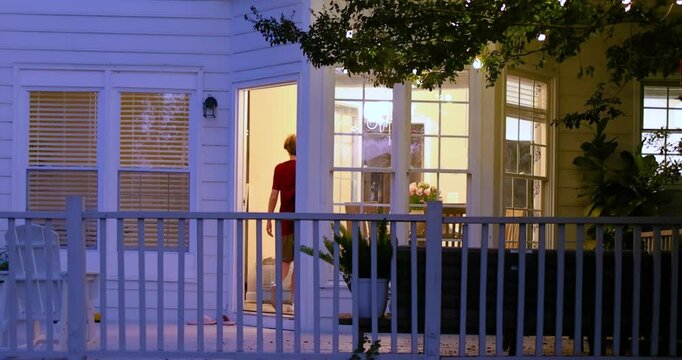 Teenage Boy Entering Home Through Back Terrace at Dusk &ndash; Cozy House Exterior with Warm Interior Lights