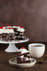 Piece of Black forest cake with cherry, cream with shea butter, cognac and chocolate biscuit on a wooden table. Vegan dessert. Vertical orientation.