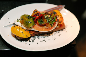 Colorful salad topping on toasted bread served with herbs, black seeds, and fresh vegetables in a dining setting