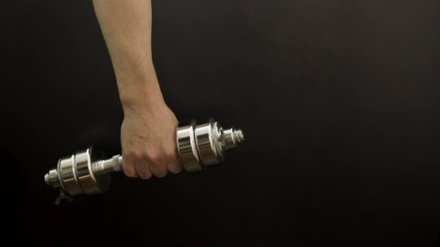 Hand rotating a dumbbell on a black background.