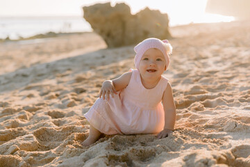 Beautiful girl in outdoor with sunset light. Child in pink dress on sandy beach.