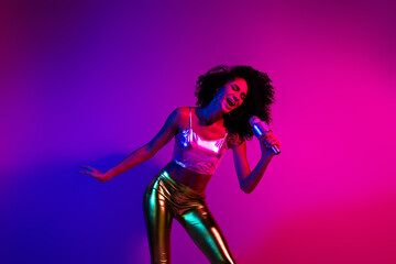 Naklejka premium Young fashionable woman singing with passion under vibrant neon lights in a purple and pink nightclub inspired setting