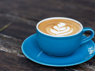 A cup of cappuccino coffee, with a blue cup placed on a black wooden table. Beautiful latte art with leaf shape.