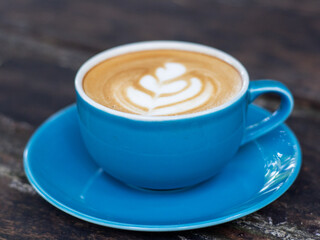 A cup of cappuccino coffee, with a blue cup placed on a black wooden table. Beautiful latte art with leaf shape.