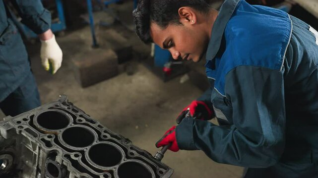 Close-up of automotive engineer loosening a nut on engine block with red gloves, focused on precision in automotive workshop, with observer in white gloves standing nearby