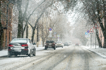 Fototapeta premium Cars parked on the side of the road in the city during a snowfall in winter