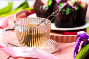 Tea in a glass cup with a saucer on a light background, next to muffins with candied fruits and...