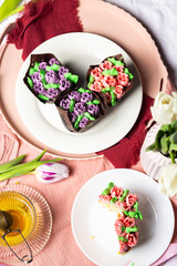 Muffins with candied fruits and cream in the form of tulips on a white plate, homemade pastries for Mother's Day, light composition, muffins with tea, tulips and pink silk ribbons in the background