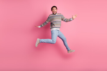 Happy young man jumping with excitement in casual funky sweater on pink background