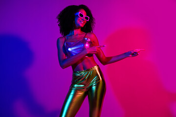 Young stylish woman dancing under vibrant neon lights in purple and pink tones expressing joy and confidence
