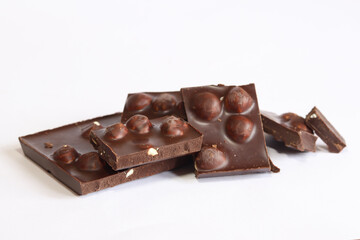 Pieces of dark chocolate with nuts on a white background. Food concept, sweets. Chocolate with whole hazelnuts. Pieces of dark chocolate with hazelnuts. Dessert