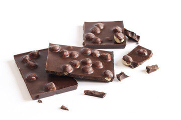 Pieces of dark chocolate with nuts on a white background. Food concept, sweets. Chocolate with whole hazelnuts. Pieces of dark chocolate with hazelnuts. Dessert