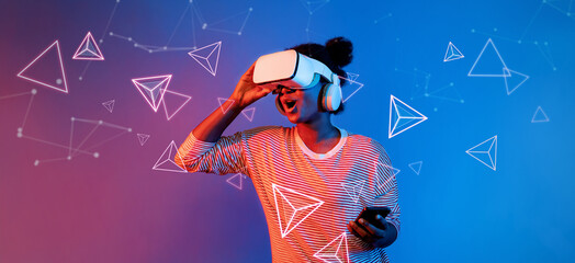 African girl with VR glasses standing at blue and pink background and looking at floating geometric shape. Excited person searching and entering visual reality world. Technology innovation. Ingenuity.