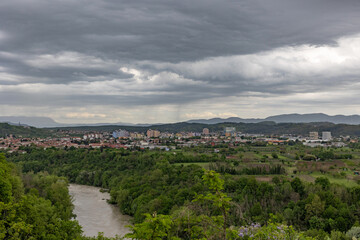 vista con al centro l'ambiente urbano della città di Nova Gorica, in Slovenia, vicina al fiume Isonzo, con sullo sfondo montagne e colline, sotto un cielo coperto da nuvole grigie, in estate