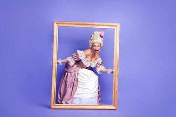Woman in elegant baroque attire posing humorously in a picture frame against violet background