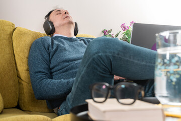 Obraz premium Man relaxing on couch with headphones, listening to music and unwinding