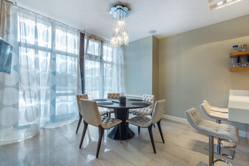 The interior of the kitchen and dining room in a private house. Panoramic window. Beige chairs at the round table.