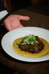 a waiter is serving a red meat steak with mashed potatoes on a white plate on a brown table 