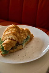 a croissant sandwich on a white plate on a table next to a red sofa