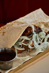 meat with onions in a flat bread with sauce on a white table next to a red sofa