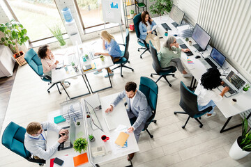Modern open-plan office with diverse professionals collaborating on computers during daylight hours, top view