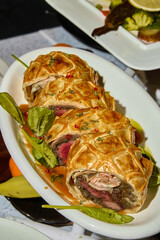 a beef wellington with sauce on a white plate 