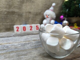 cup with pieces of marshmallows, in the background a Christmas and New Year composition with the numbers 2025