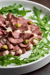 vitello tonnato salad with pork,sauce and olives on a white plate