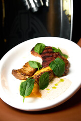 a red meat steak with vegetables and sauce on a white plate