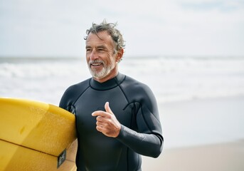 Smiling man in a wetsuit holding a yellow surfboard at the beach
