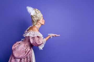 Elegant woman in royal baroque costume posing on a violet background in historical fashion attire