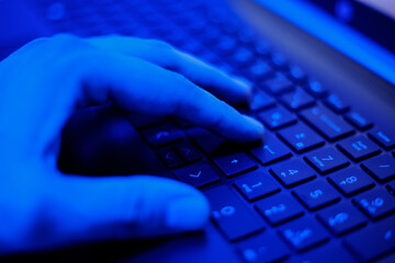 Close-Up of a Hand Typing on a Keyboard in Dim Blue Light